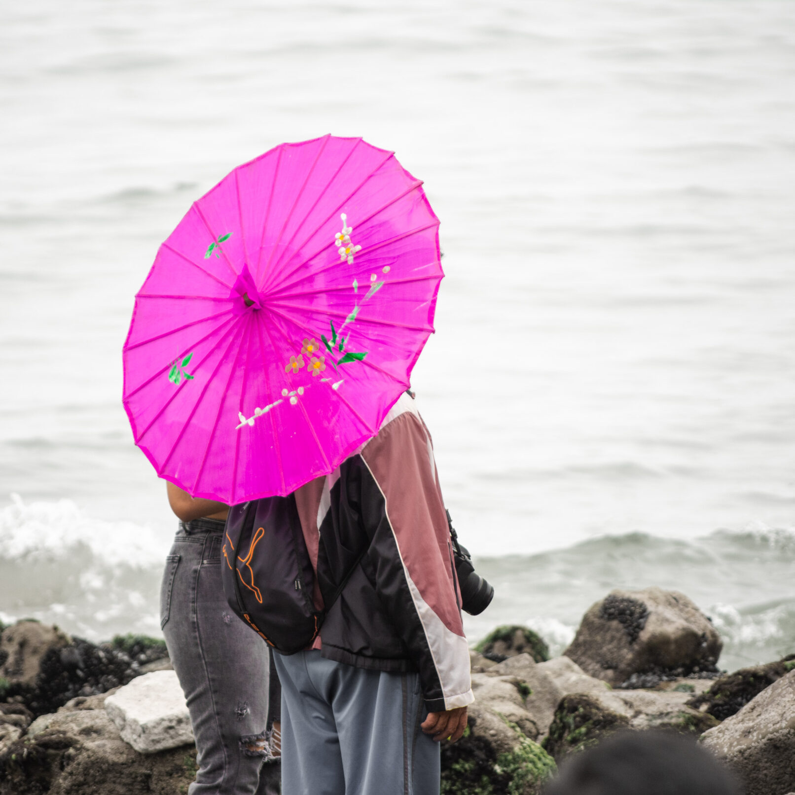 Two people on beach with pink umbrella in Lima, Peru